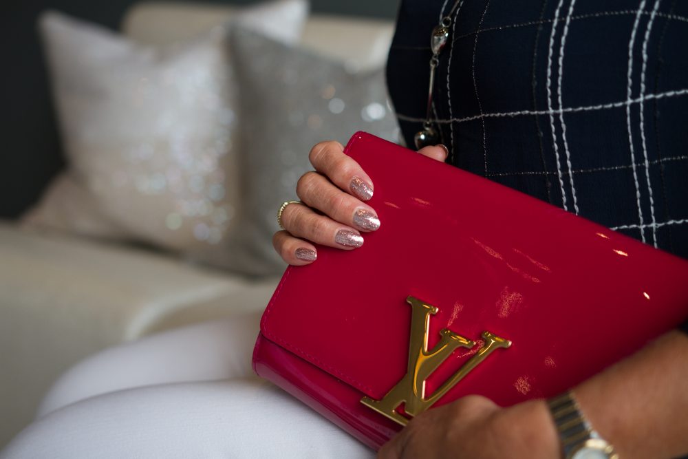 a client with glittery gel nails, holding her louis vuitton patent red clutch